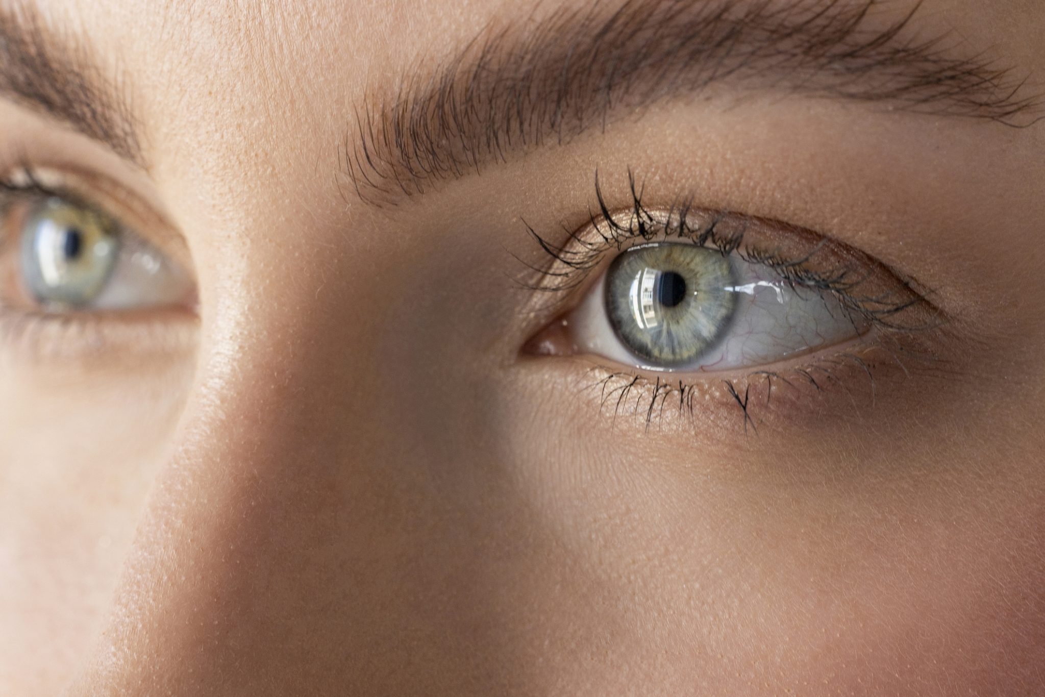 Close-up of a person's blue-green eye, long lashes, natural brows and detailed skin texture