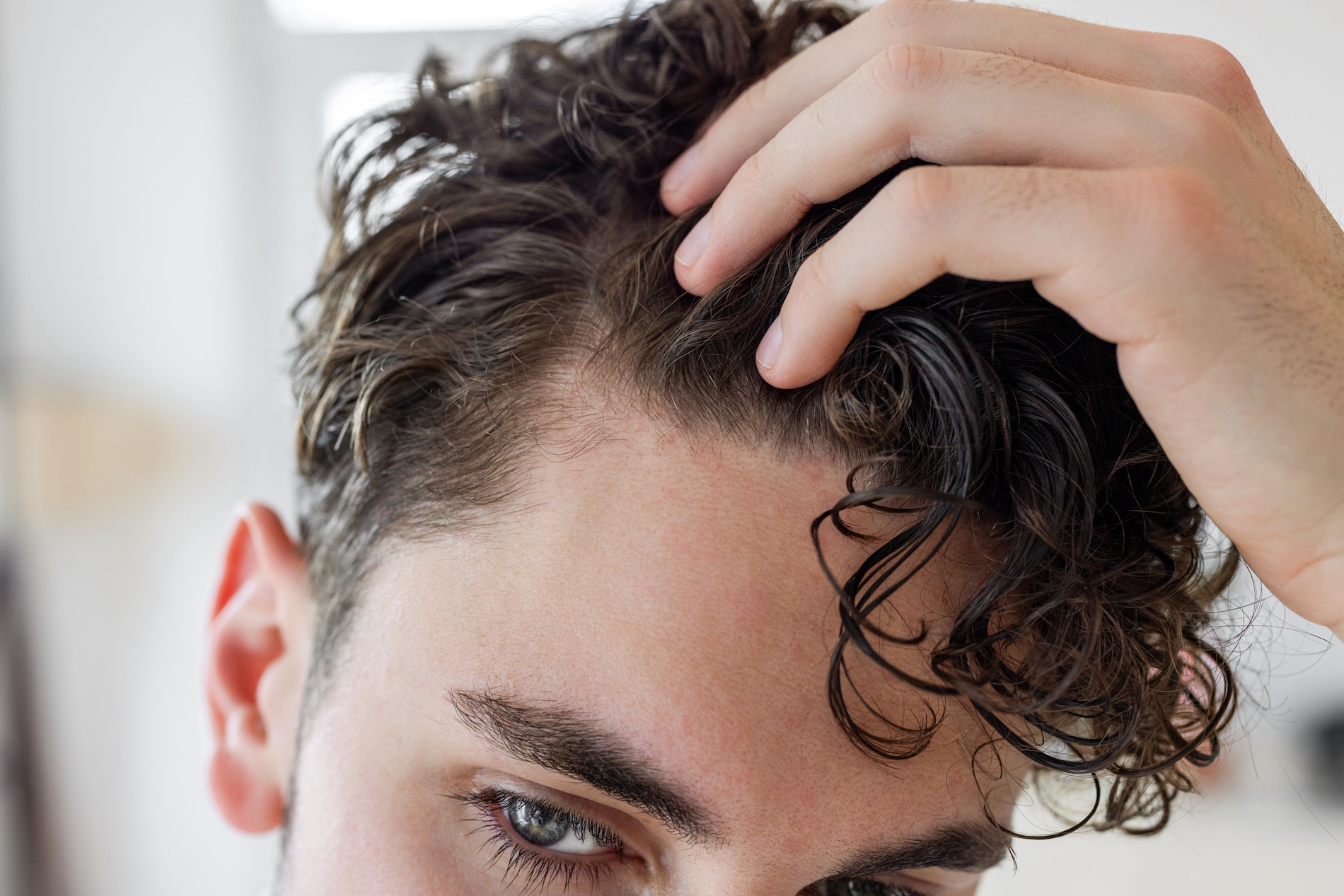 Close-up of a man checking his hairline while running fingers through curly hair
