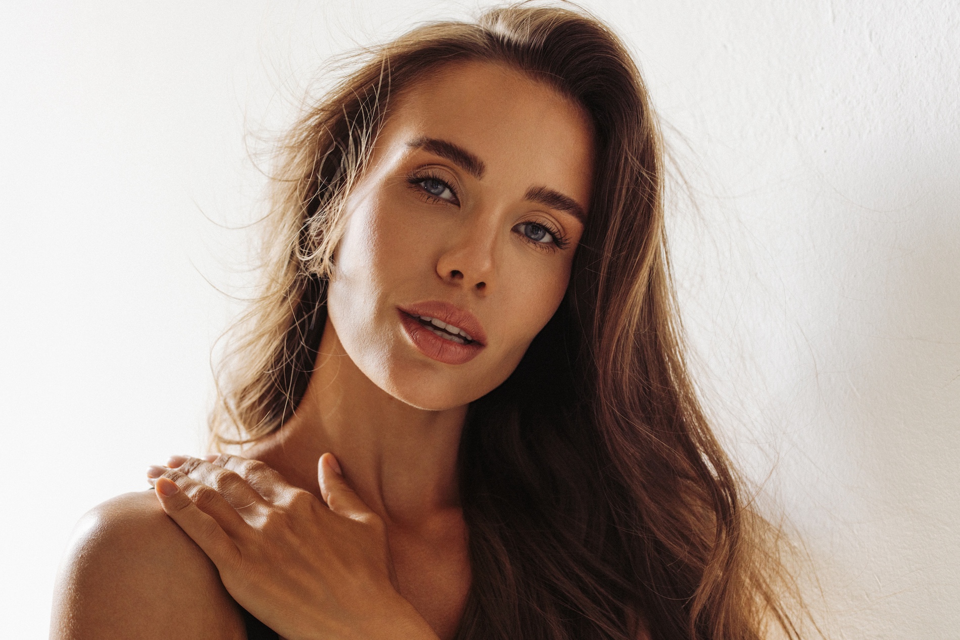 Close-up portrait of a woman with long brown hair, soft makeup, hand on her shoulder, warm natural lighting