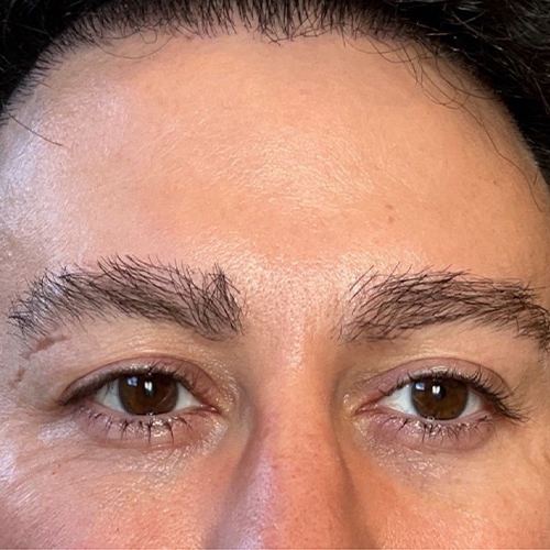 Close-up of a person's brown eyes with thick eyebrows and forehead skin texture