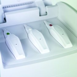 Close-up of three white dental handpieces in a charging dock with green, white, and red indicator buttons